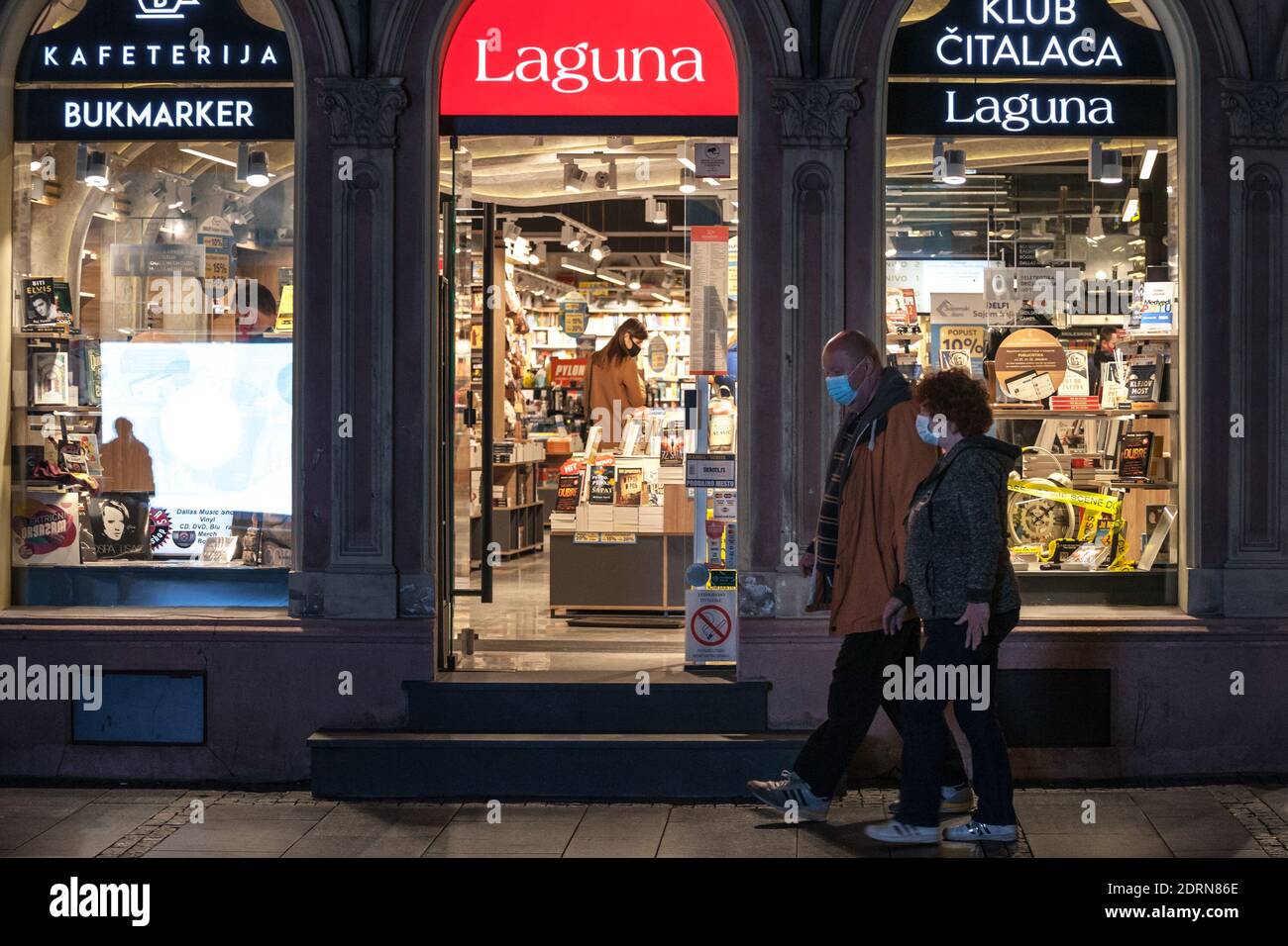 BELGRAD, SERBIEN - 21. OKTOBER 2020: Altes Seniorenpaar, das vor einer Buchhandlung vorbeikommt, wobei Kunden Bücher auswählen, die eine Atemmaske tragen Stockfoto