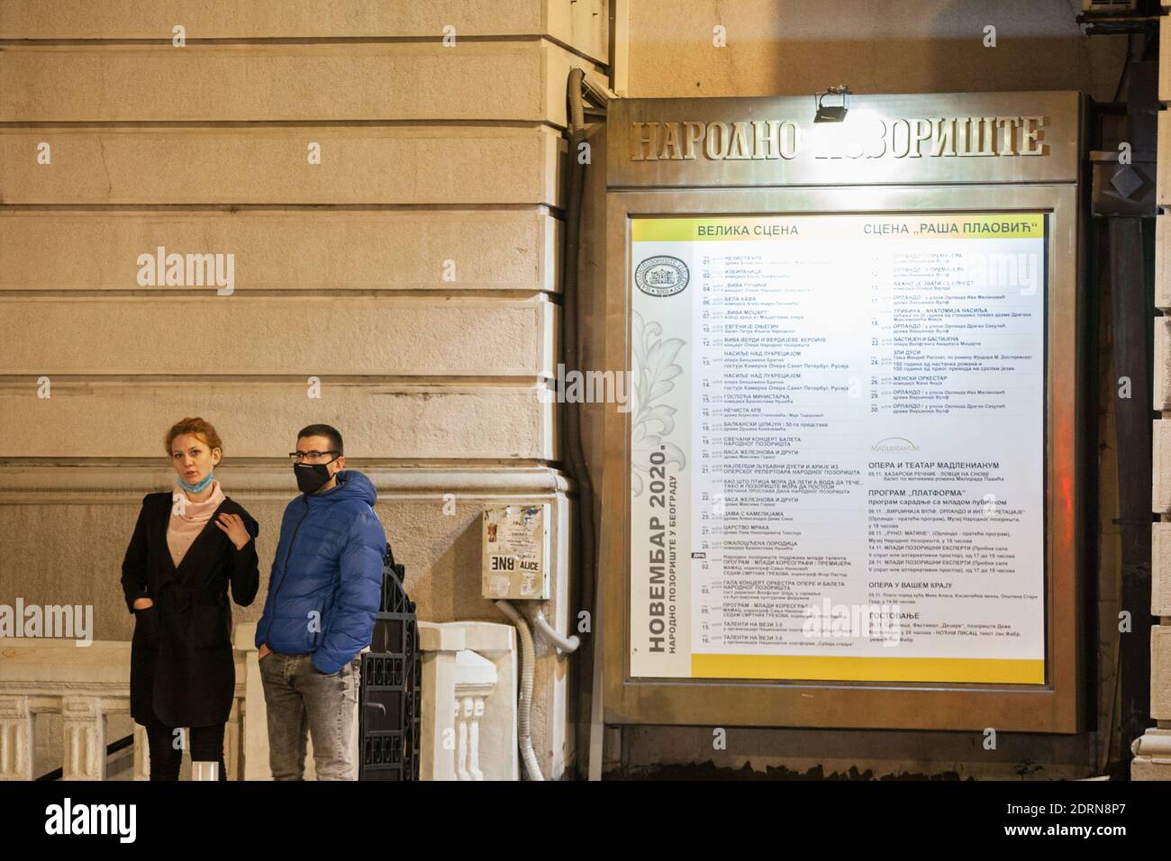 BELGRAD, SERBIEN - 4. NOVEMBER 2020: Junge Leute, ein Paar, das vor dem Programm von Narodno pozoriste, dem Nationaltheater, steht und das Fa Stockfoto