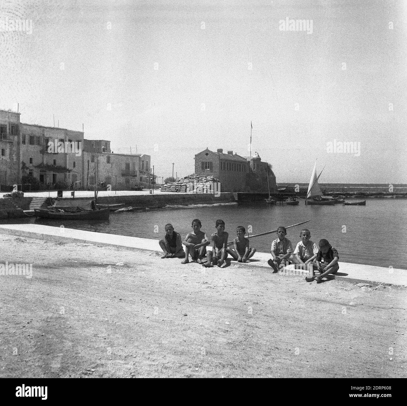 1950er Jahre, historisch, eine Gruppe von jungen Jungs, die im Hafen von Kyrenia auf Zypern sitzen. Ein alter Hafen aus dem 10. Jahrhundert v. Chr., liegt an der Nordküste der Insel und ist nur 40 Meilen vom türkischen Festland entfernt und war ein wichtiger Halt auf Handelsrouten. Stockfoto