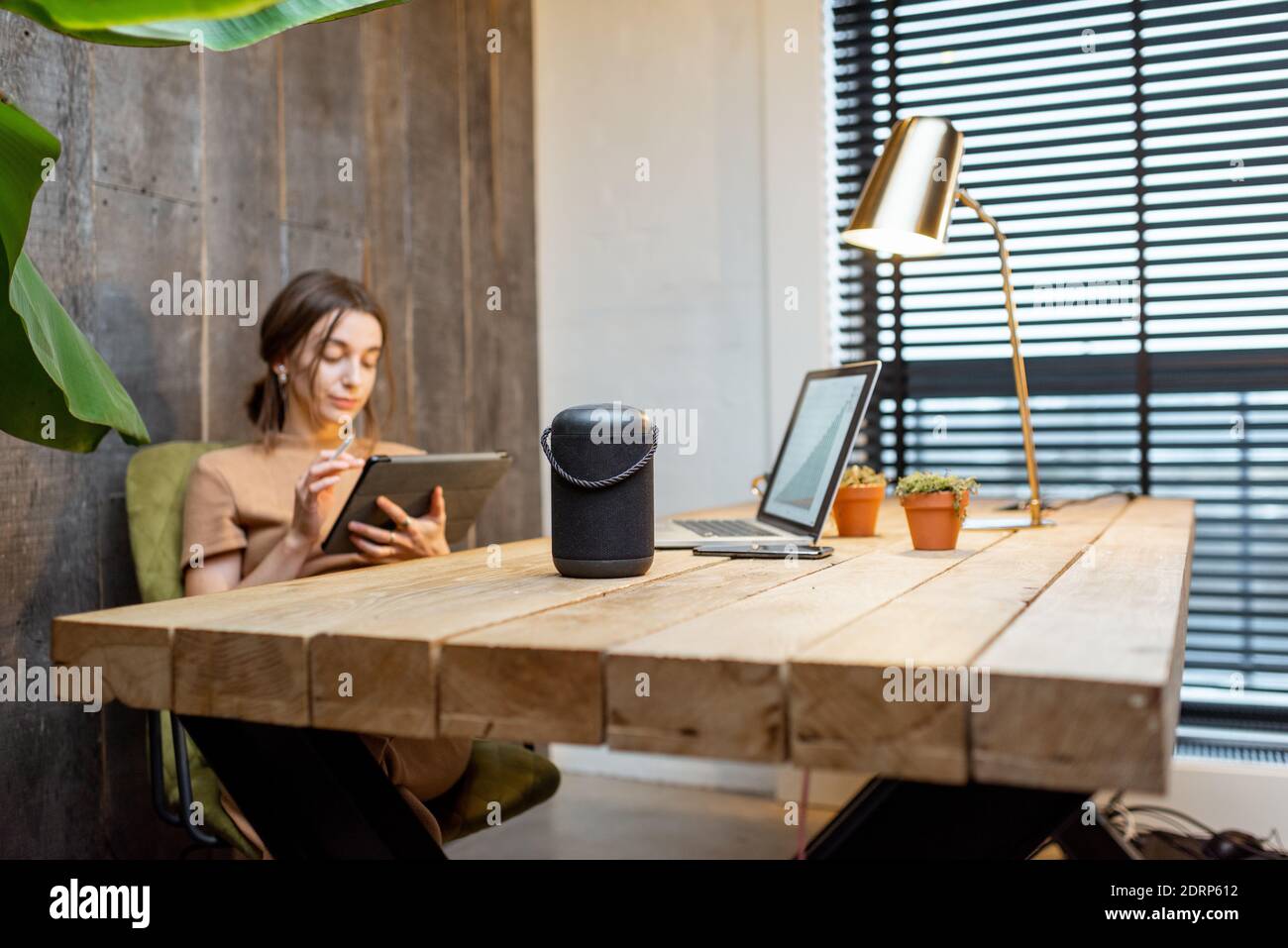 Frau, die im gemütlichen Home Office am digitalen Tablet arbeitet. Intelligenter Lautsprecher auf dem Tisch. Konzept eines Smart Home und Arbeit von zu Hause aus Stockfoto