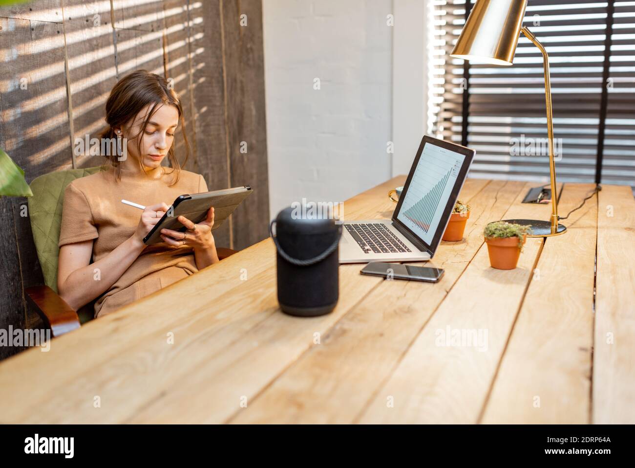 Frau, die im gemütlichen Home Office am digitalen Tablet arbeitet. Intelligenter Lautsprecher auf dem Tisch. Konzept eines Smart Home und Arbeit von zu Hause aus Stockfoto