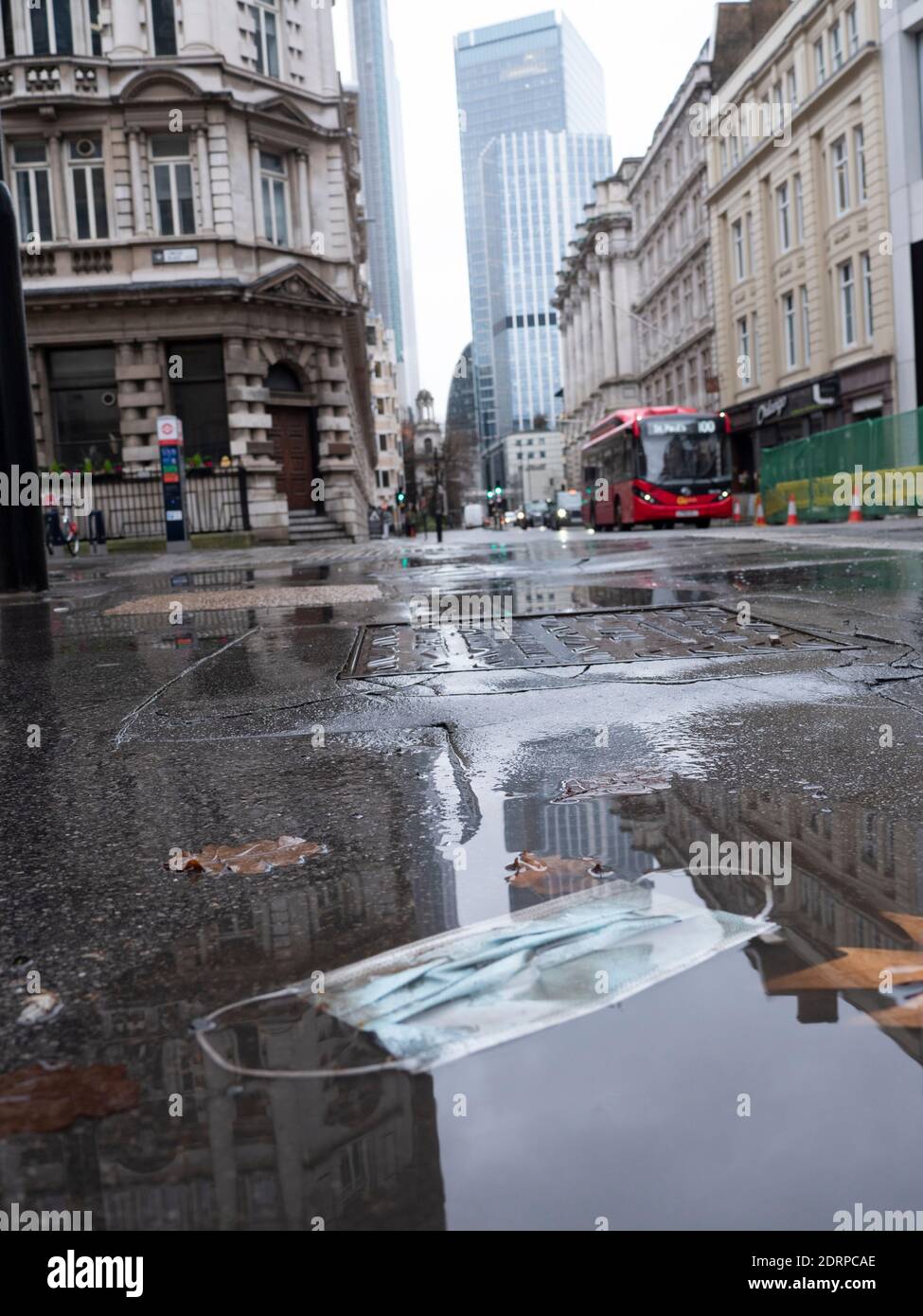 Die PSA-Maske liegt in einer Pfütze während des Regens an der London Wall, einer normalerweise geschäftigen, aber jetzt ruhigen, leeren Hauptstraße in der City of London während der Covid Coronavirus Pandemie Stockfoto