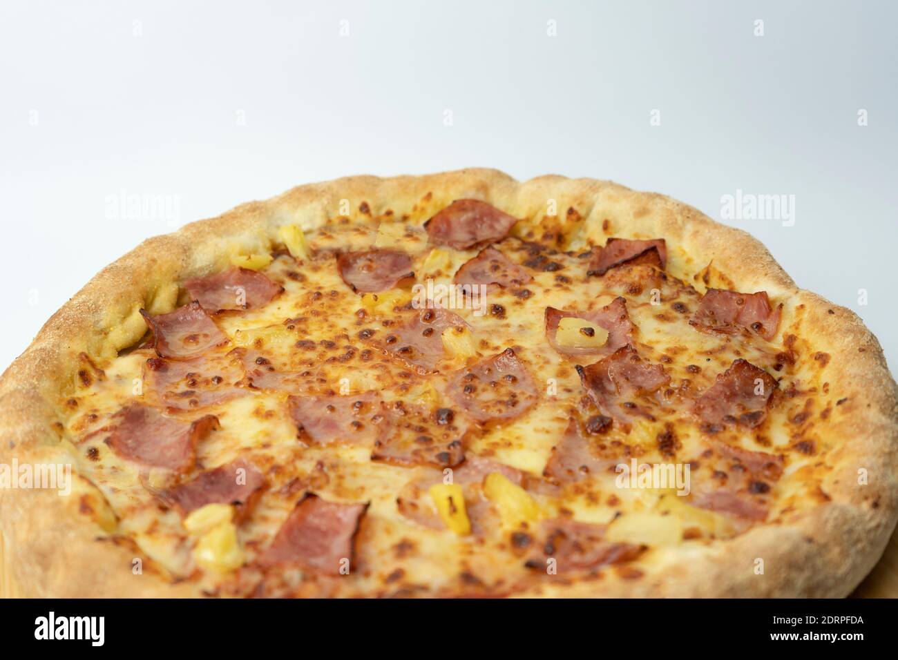 Pizza mit Käse, knusprigem Speck und Ananas auf Holzpizzabrett und weißem Hintergrund.Hawaiianische Pizza mit Kopierraum für Text, Restaurant Essen Konz Stockfoto