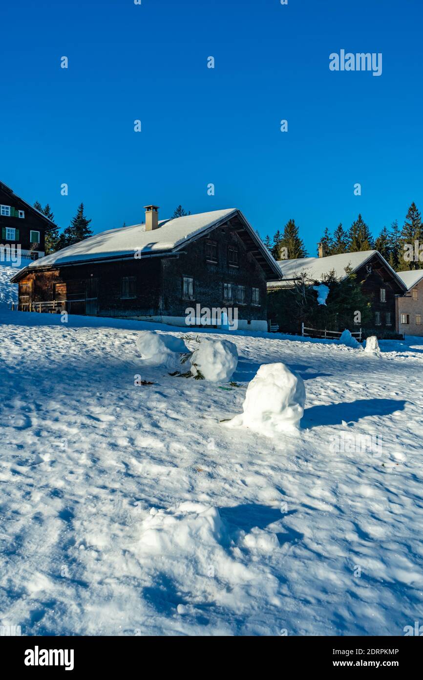 kleine Schneemänner auf einer Alp. almhütte mit Schneemanen. Winterlicht auf einem Almhof. Verschneite Landschaft in den Bergen Vorarlbergs Stockfoto