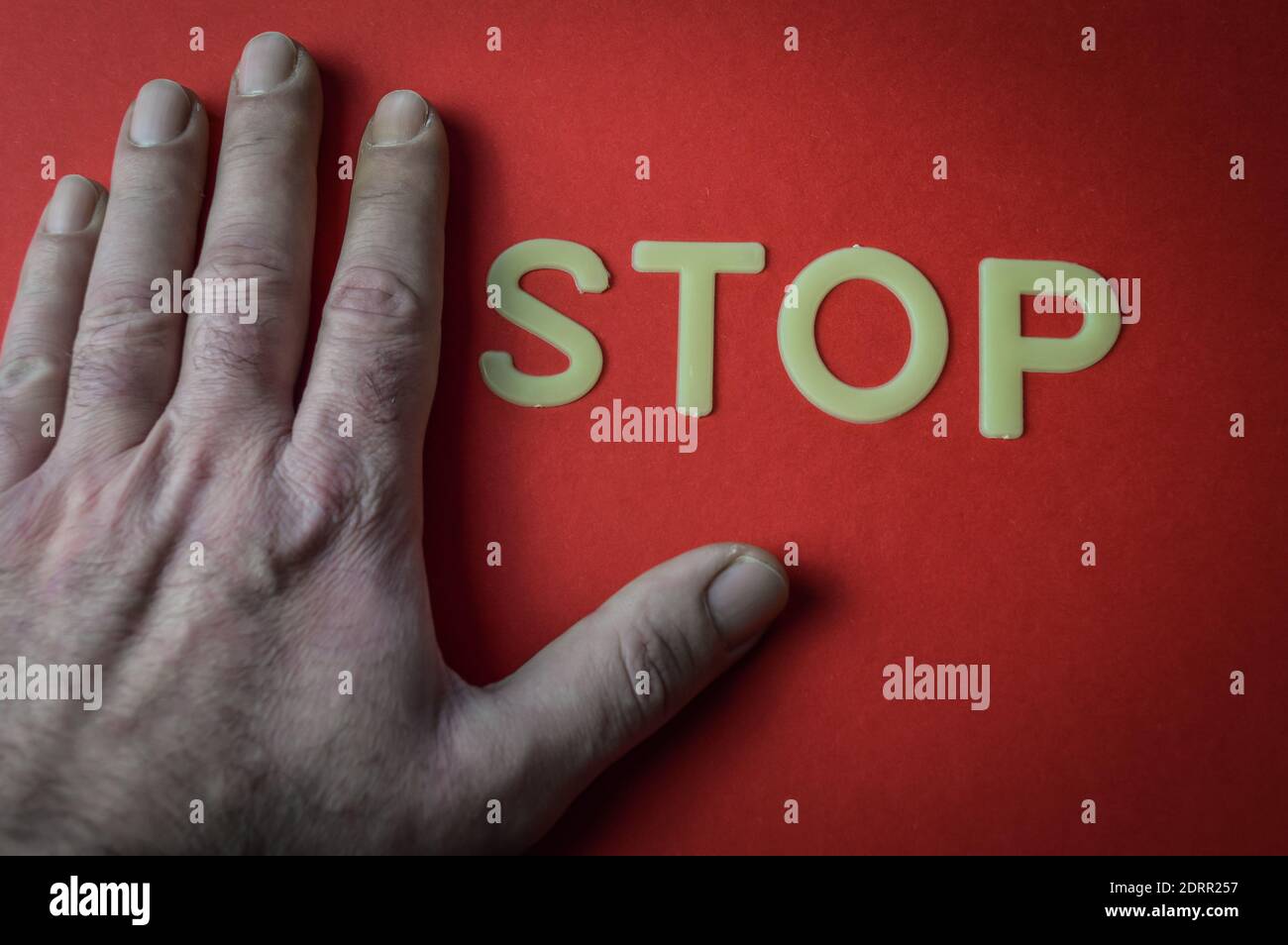 Menschliche Hand neben dem Wort Stop geschrieben mit Plastikbuchstaben auf rotem Papierhintergrund, Konzept Stockfoto