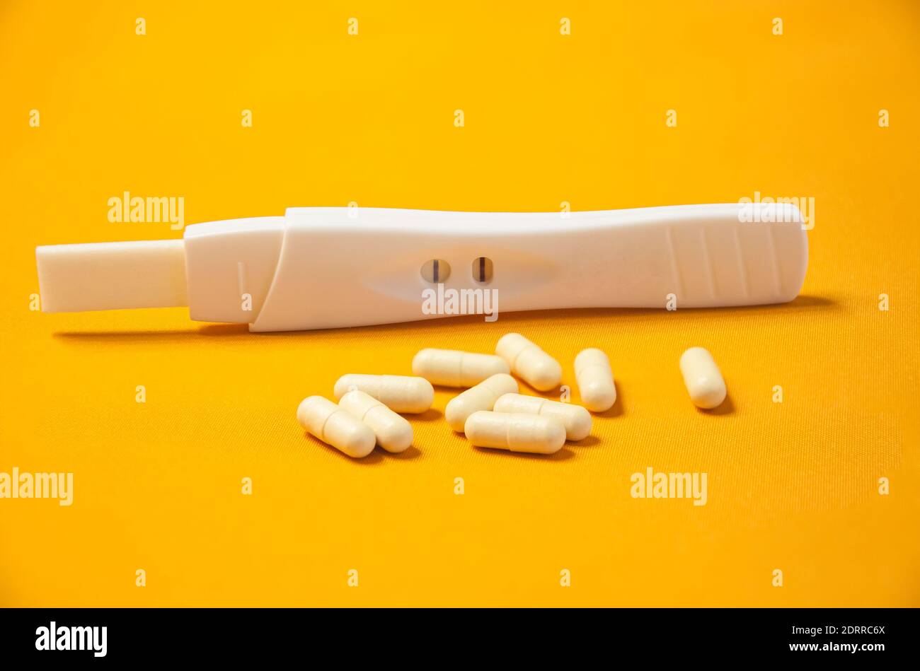 Ein Schwangerschaftstest mit einem positiven Ergebnis und einer Handvoll Pillen auf gelbem Hintergrund. Das Konzept der Verhinderung unerwünschter Schwangerschaft Stockfoto