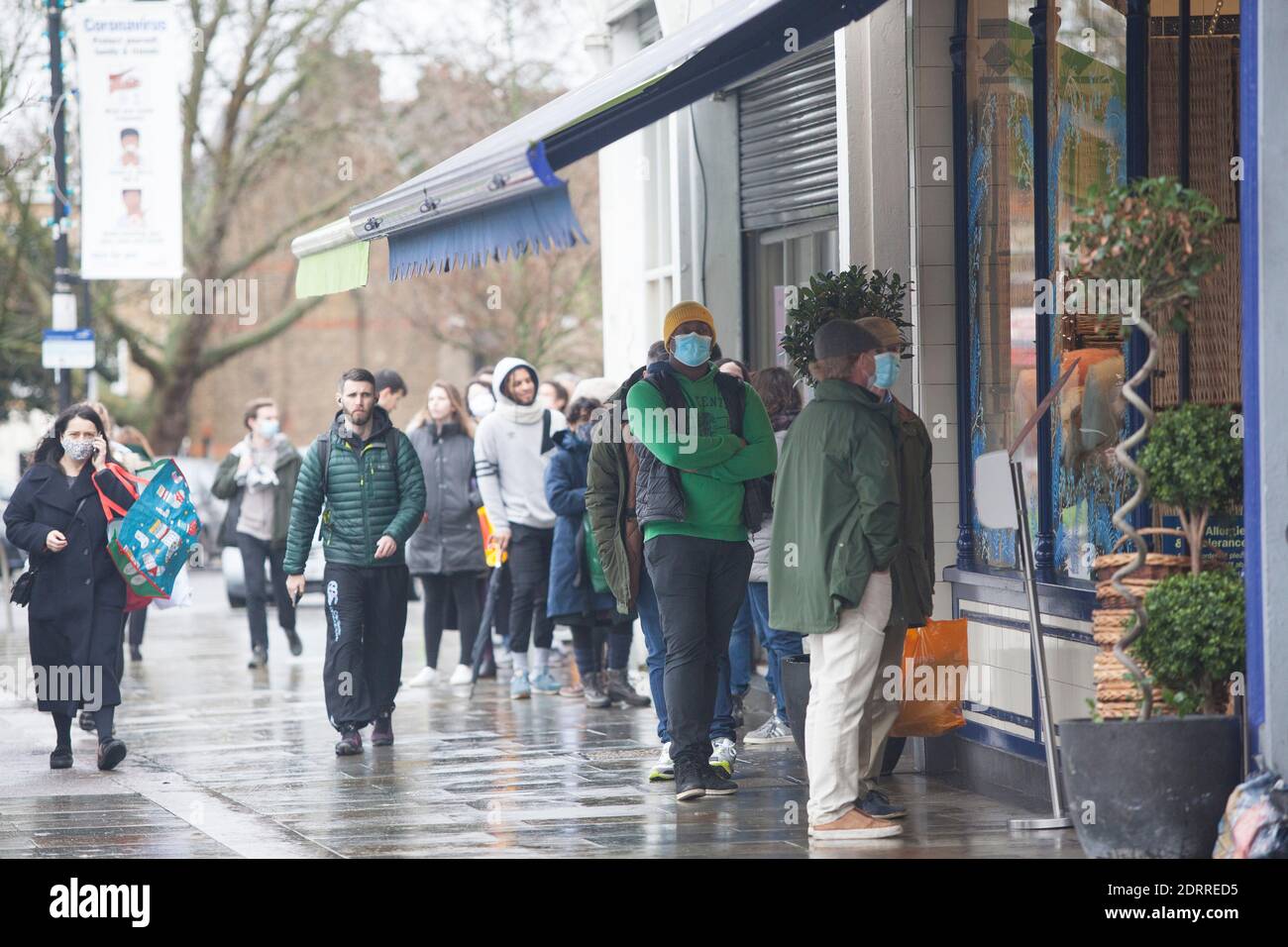 Clapham, London, 21. Dezember 2020: Im Regen stehen die Leute Schlange, um Weihnachtsaufträge von einem lokalen Metzger zu sammeln. Unter Tier 4 Coronavirus Einschränkungen sollten die Menschen zu Hause bleiben, außer für wesentliche Einkäufe und zur Arbeit zu gehen. Cafés und Restaurants sind nur für Essen zum Mitnehmen geöffnet und Deliveroo liefert Lebensmittel sowie warme Mahlzeiten. Anna Watson/Alamy Live News Stockfoto