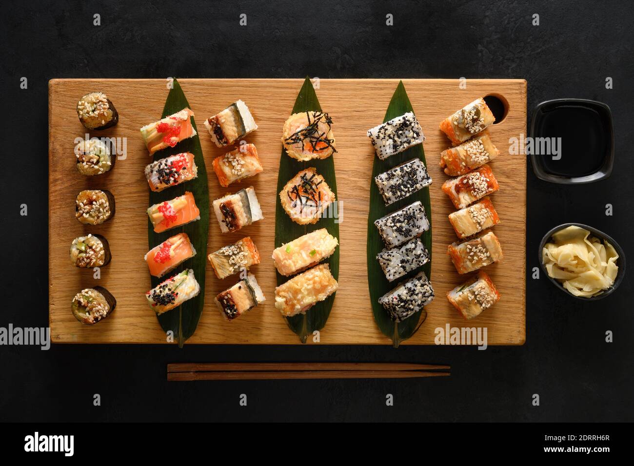 Sushi-Set auf Holzbrett auf schwarzem Hintergrund serviert. Blick von oben. Flache Lay-Optik. Stockfoto