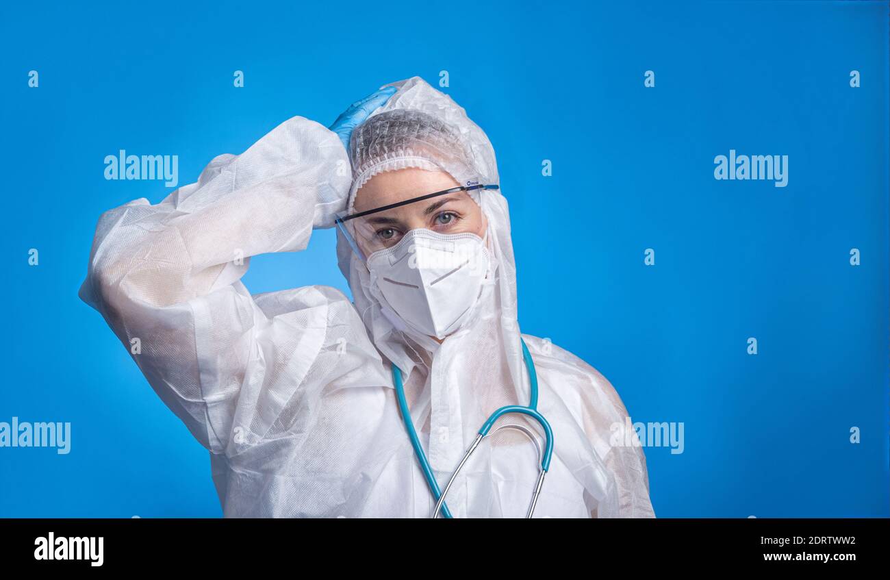 Porträt einer müden Ärztin, die Schutzanzug trägt, um gegen die Coronavirus-Pandemie zu kämpfen covid-2019. Doktor Porträt auf blauem Hintergrund Stockfoto