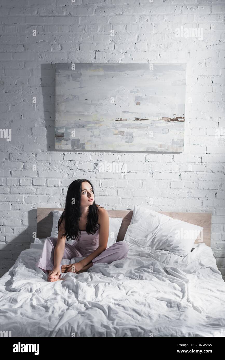 Junge Brünette Frau sitzt im Bett am Morgen Stockfoto
