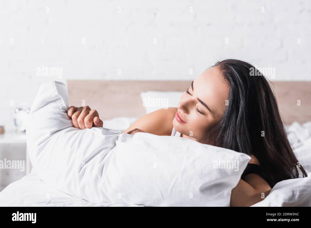 Junge Brünette Frau im Bett mit Kissen Stockfoto