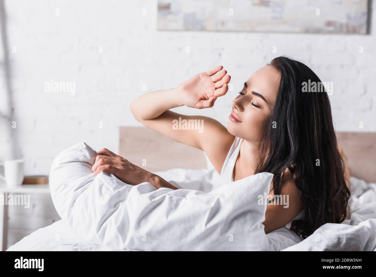 Junge Brünette Frau im Bett gegen Sonnenlicht Stockfoto