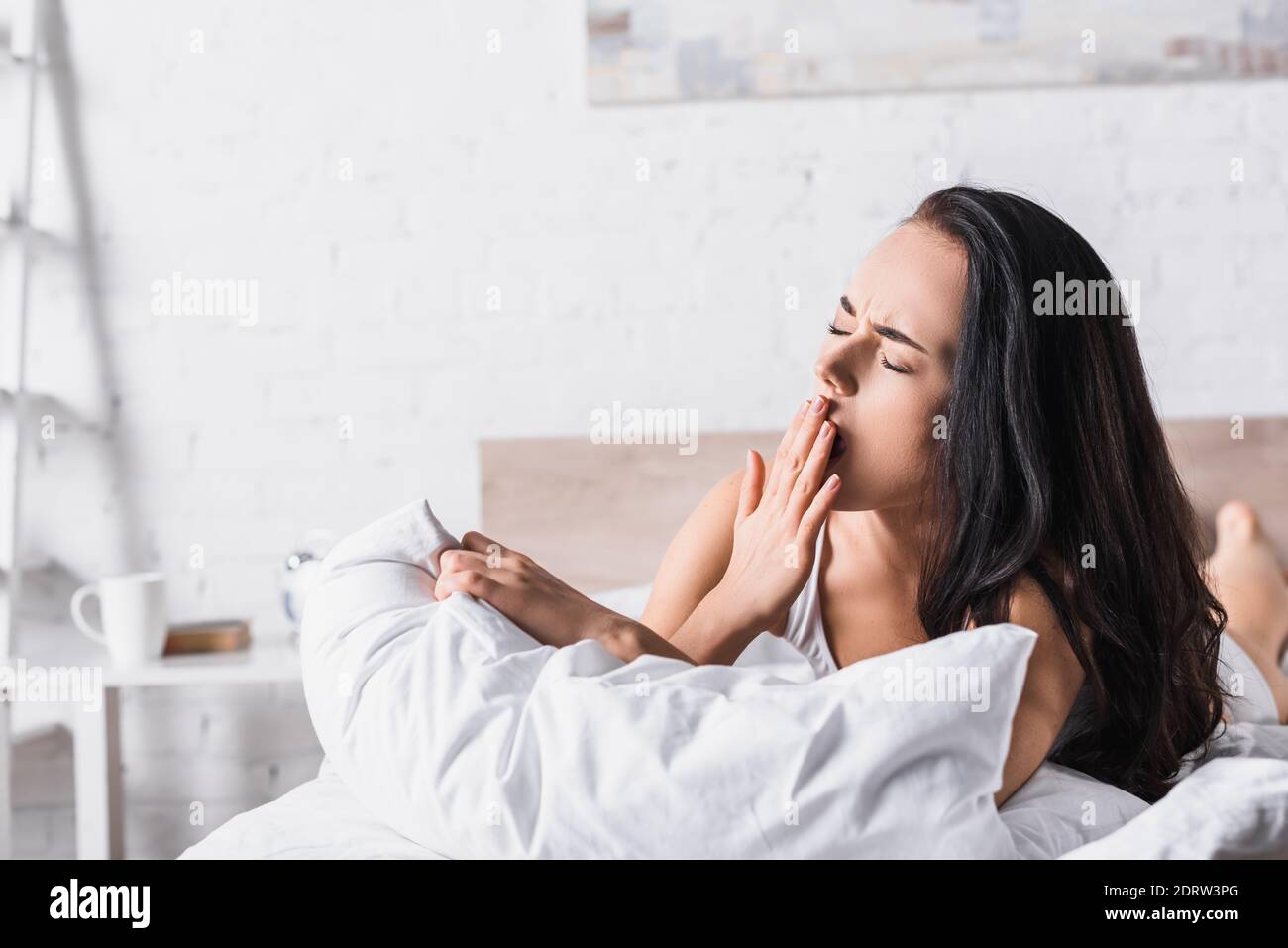Junge Brünette Frau Gähnen im Bett Stockfoto
