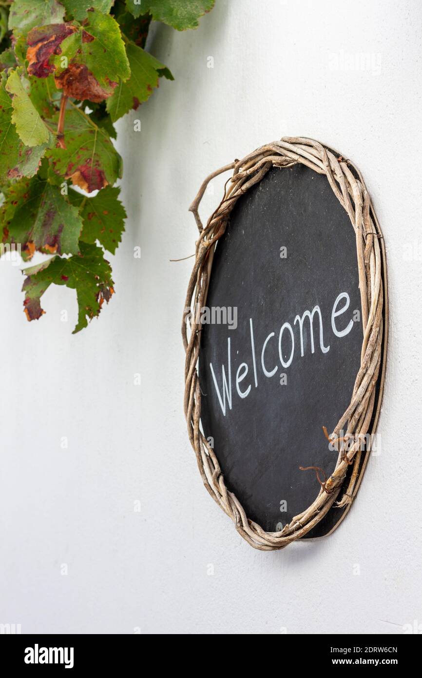 "Welcome" Schild auf schwarzem Brett mit Holzbordüre, an einer weißen Wand in einem traditionellen Haus in Santorini Insel, Griechenland, Europa. Stockfoto