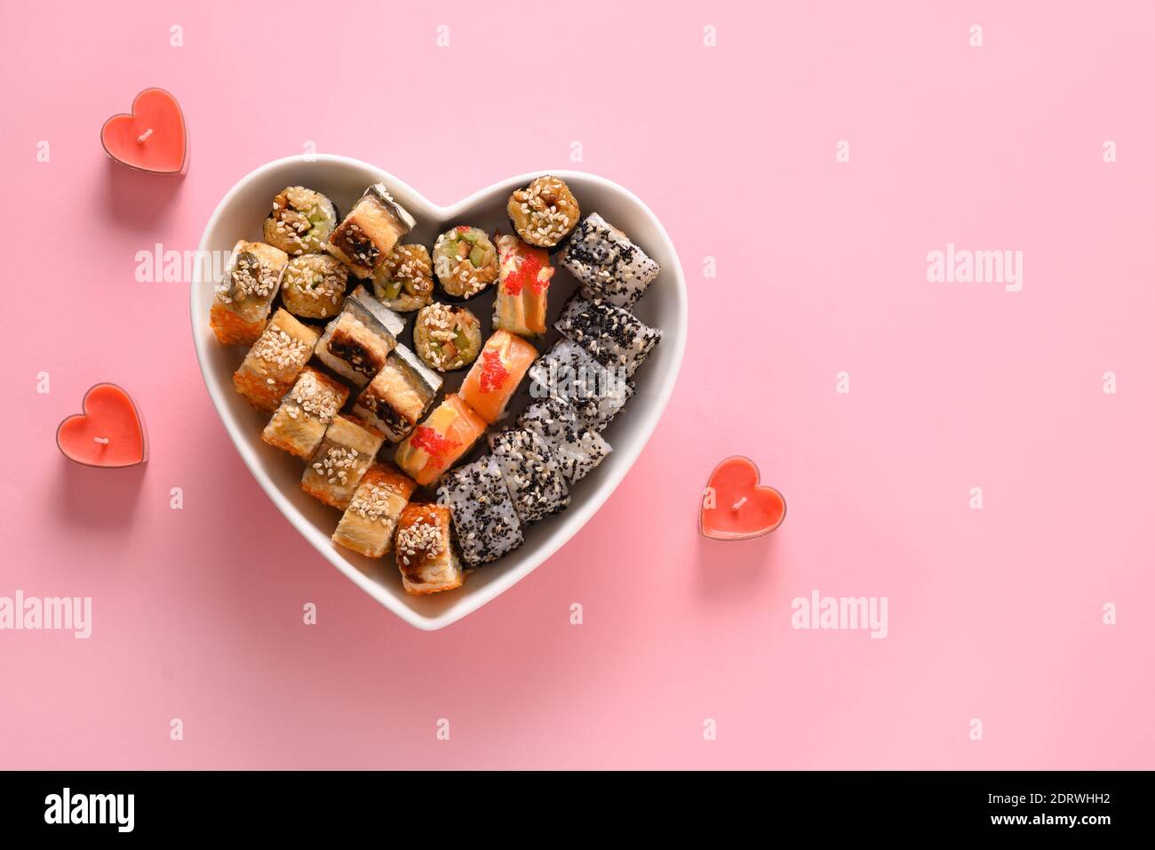Sushi in Teller als Herz auf rosa Hintergrund gesetzt. Valentine Day Food Konzept. Blick von oben. Leerzeichen für Text. Flatlay-Style. Stockfoto