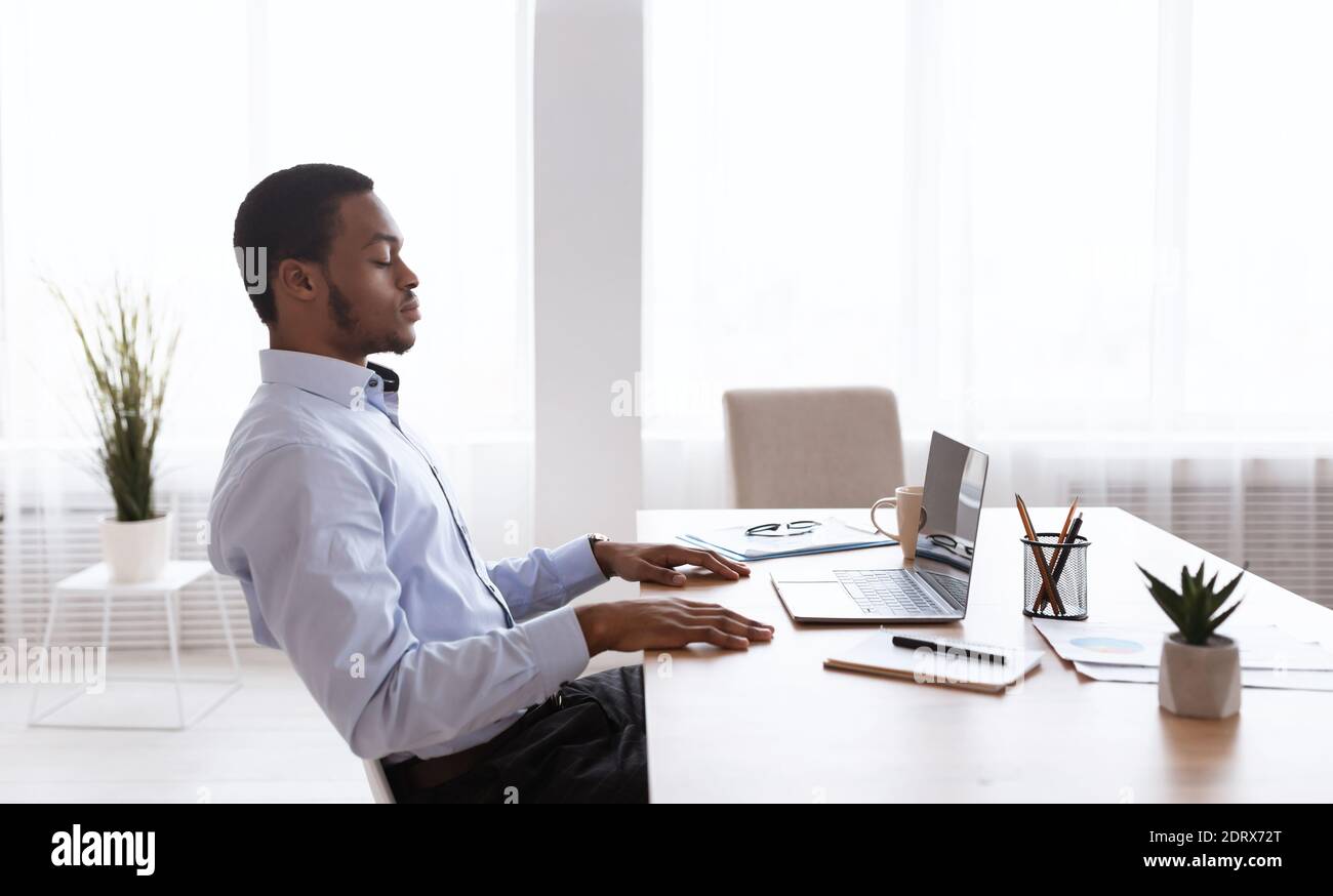 Schwarzer Geschäftsmann sitzt vor dem Laptop mit geschlossenen Augen Stockfoto