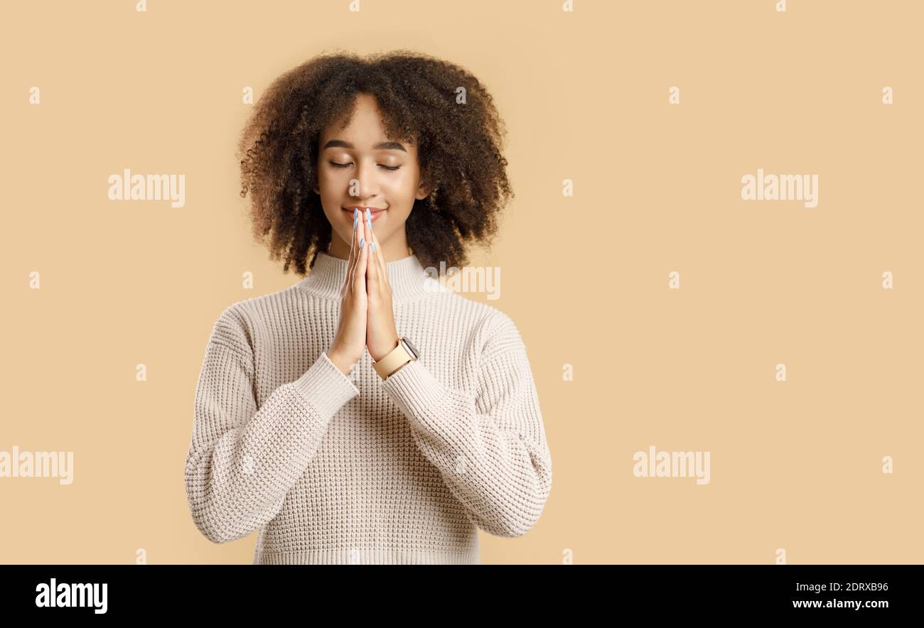 Große Bitte, Wunsch oder Traum. Befriedete junge afroamerikanische Frau mit lockigen Haaren im Pullover Stockfoto