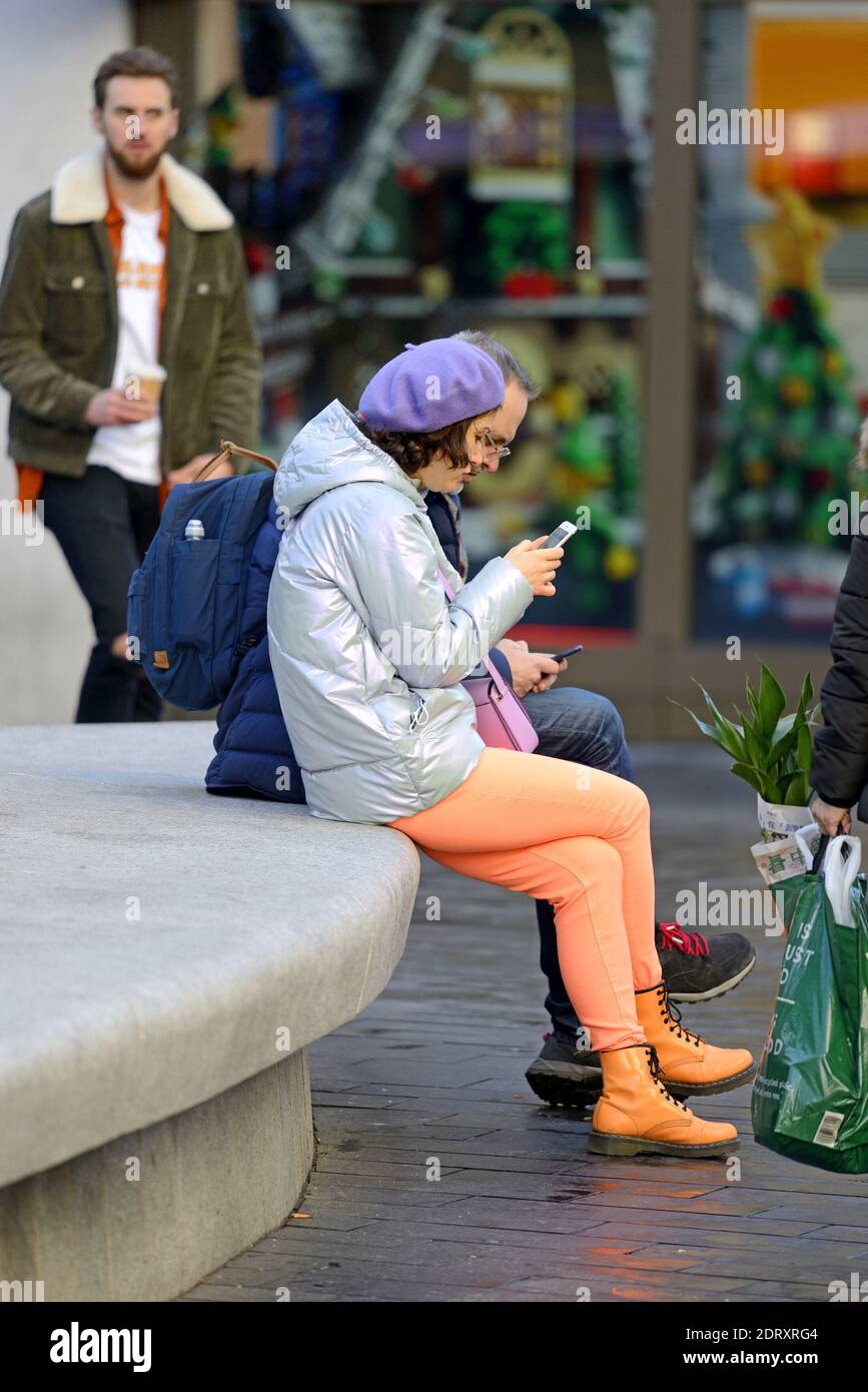 London, England, Großbritannien. Frau trägt leuchtend orange / Pfirsich Leggings und Turnschuhe, auf ihrem Handy in Leicester Square Stockfoto