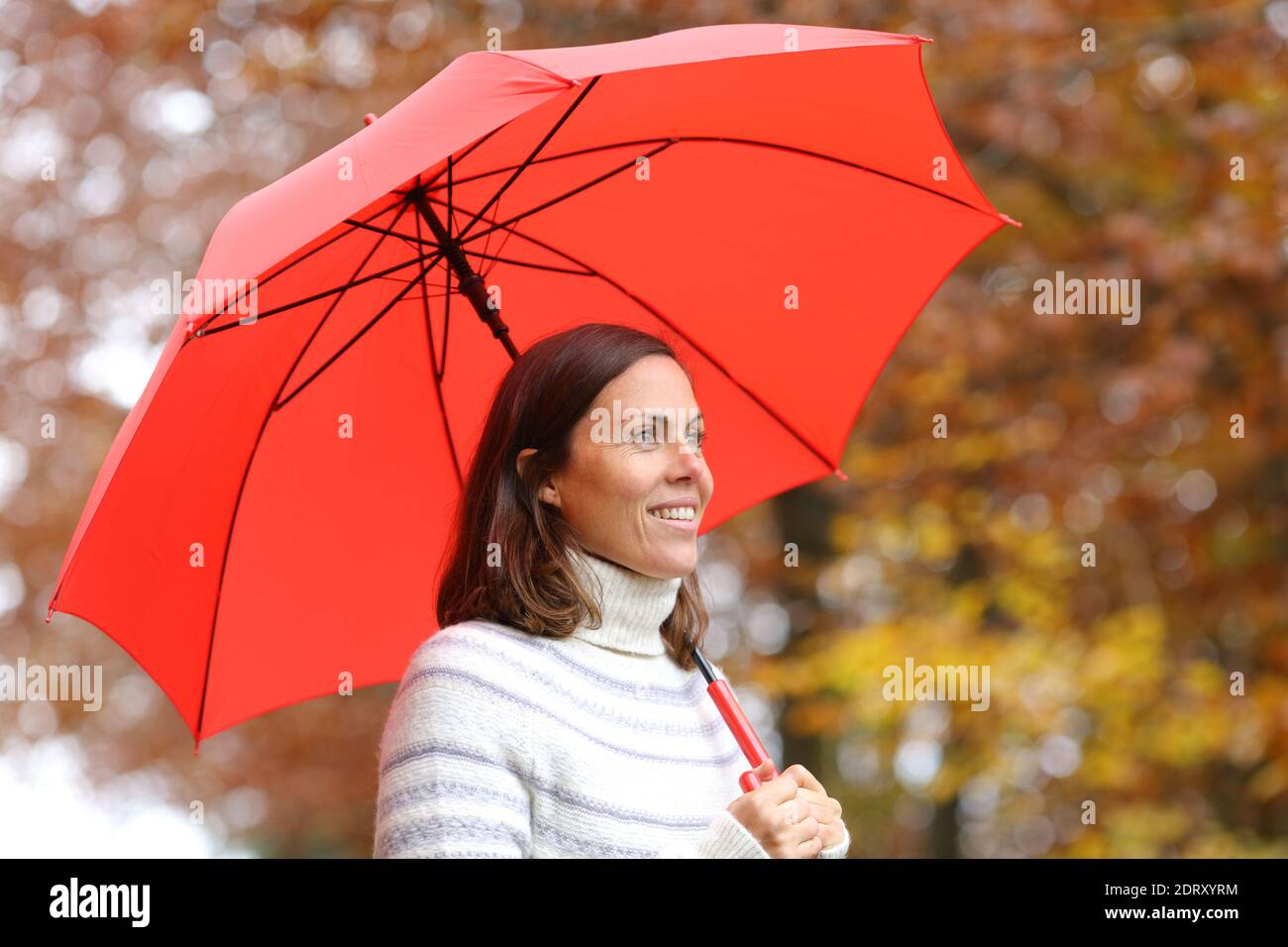 Glückliche Erwachsene Frau unter rotem Regenschirm Blick im Herbst In einem Park Stockfoto