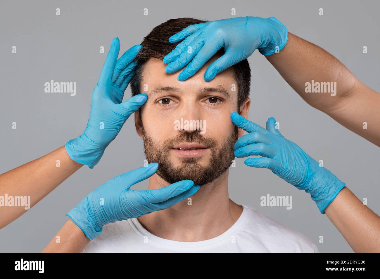 Plastischer Chirurg Hände in Schutzhandschuhen berühren mittleren Alters Mann Gesicht Stockfoto