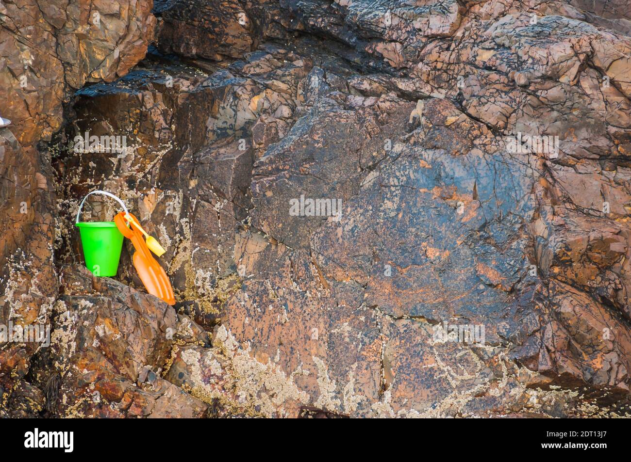 Orangefarbene Schaufel und grüner Eimer im Felsen Stockfoto