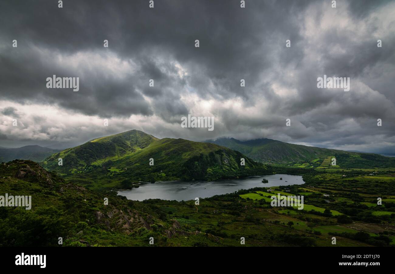 Atemberaubende Landschaft Irlands, stürmische Wolken und launischer Himmel, grüne Berge und klare tiefe See Stockfoto
