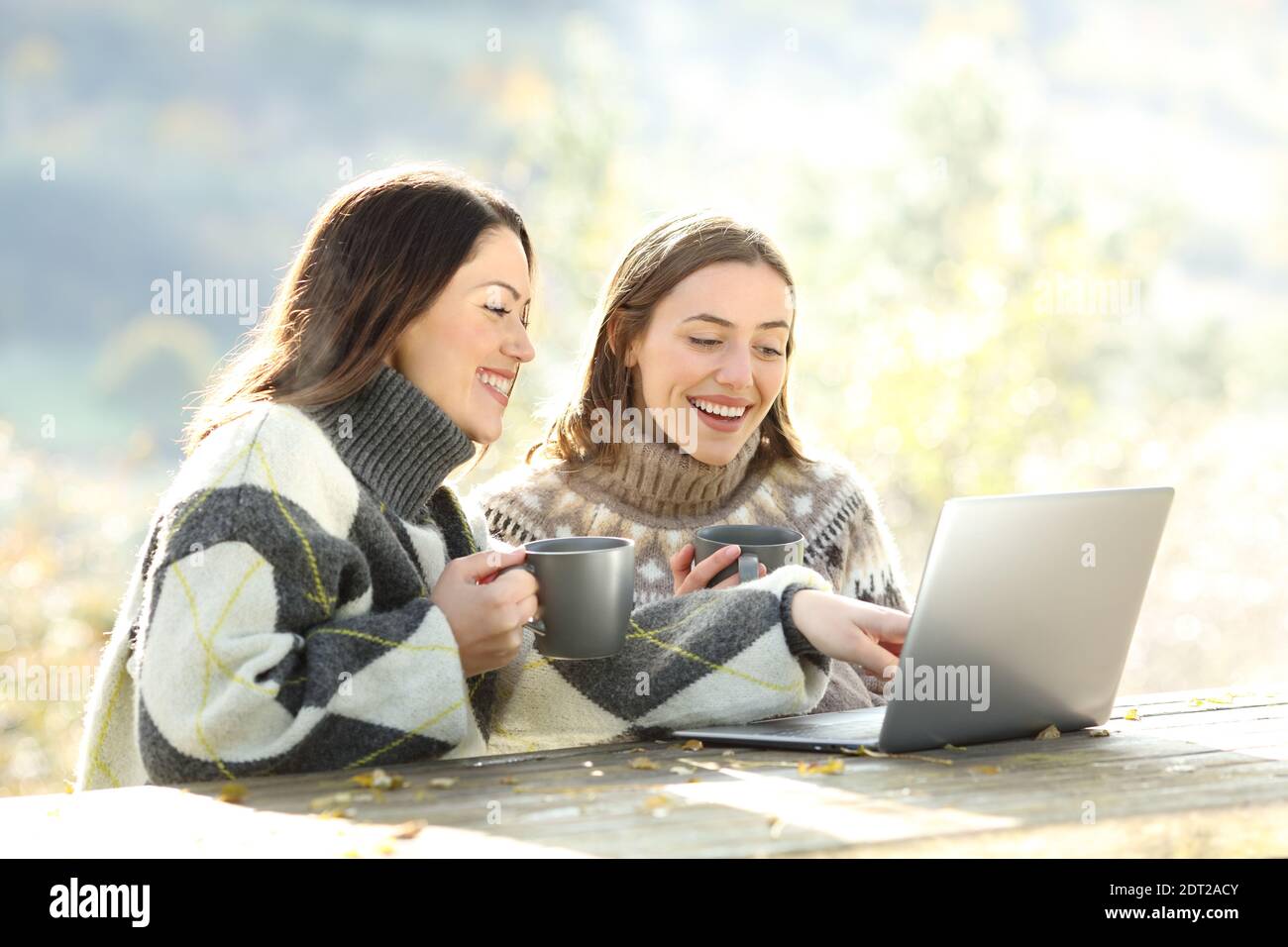 Zwei glückliche Freunde mit Laptop im Winter sitzen in einem parkbank Stockfoto