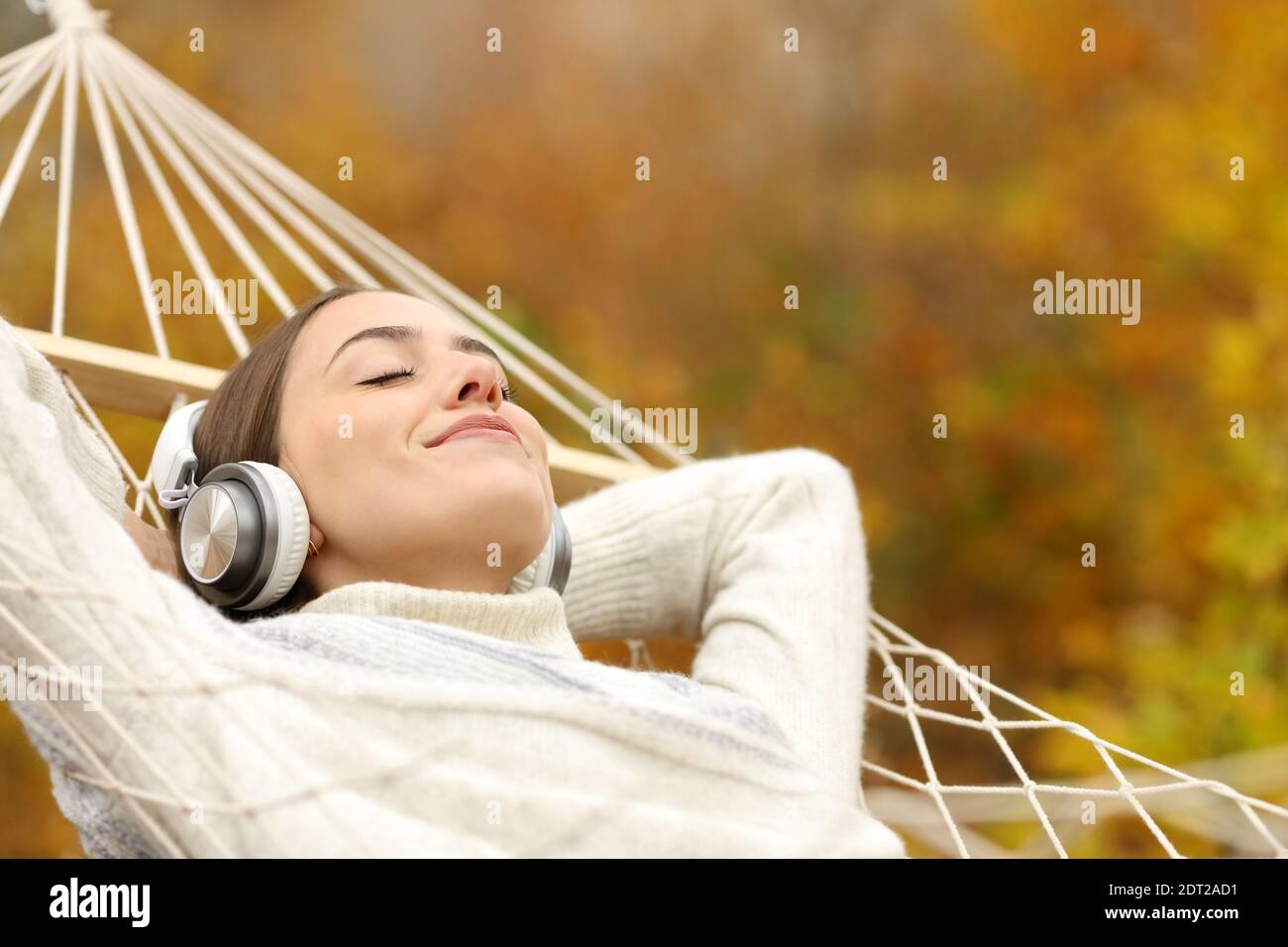 Entspannte Frau, die Musik hört, mit Kopfhörern, die in der Hängematte liegen Im Herbst im Wald Stockfoto