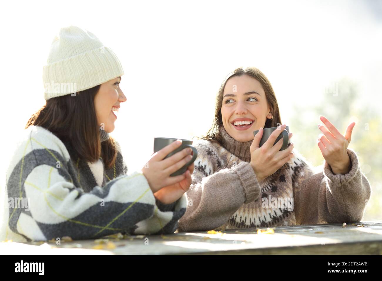 Zwei Freunde reden und lachen trinken Kaffee sitzen in der Morgen im Winter in einem Park Stockfoto