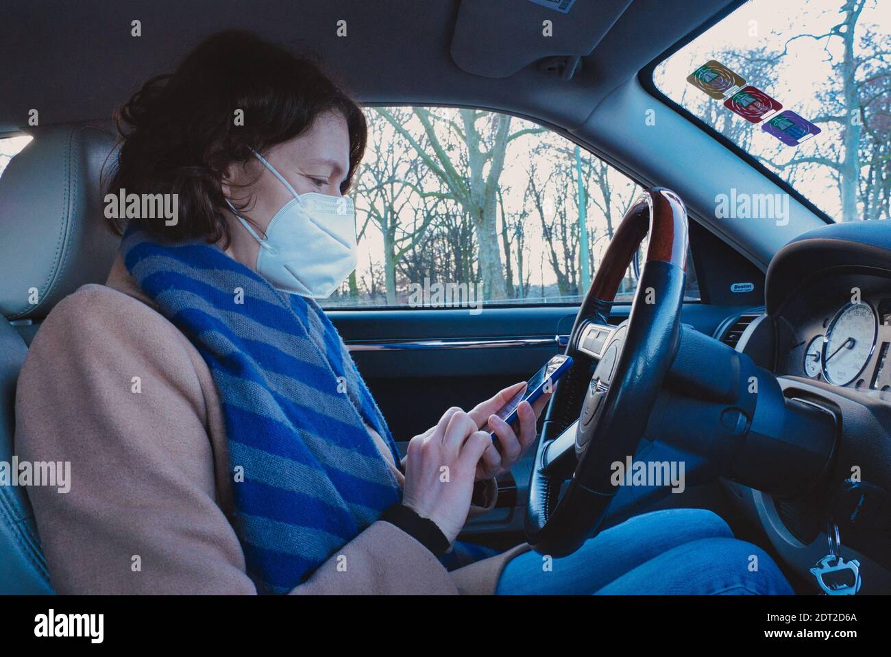 Frankfurt, Deutschland. Dezember 2020. Frau, die vom Autofahrersitz aus auf das Mobiltelefon stöbert. Profilansicht. Stockfoto