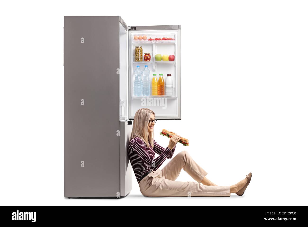 Junge Frau hält ein Sandwich und lehnt sich an einen Kühlschrank Isoliert auf weißem Hintergrund Stockfoto