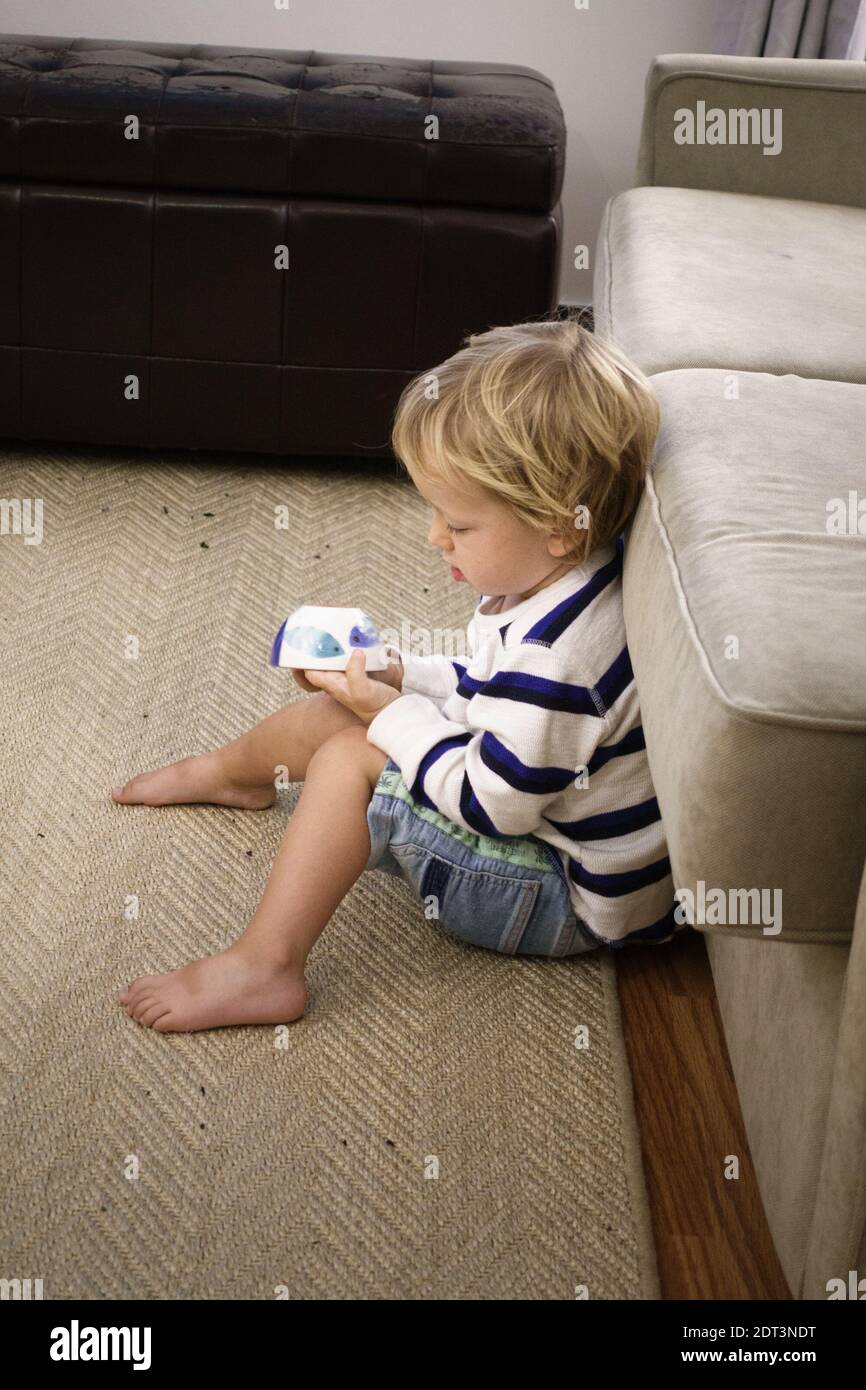 Einsamer kleiner Junge sitzt auf dem Teppich zu Hause mit Schale In der Hand Stockfoto