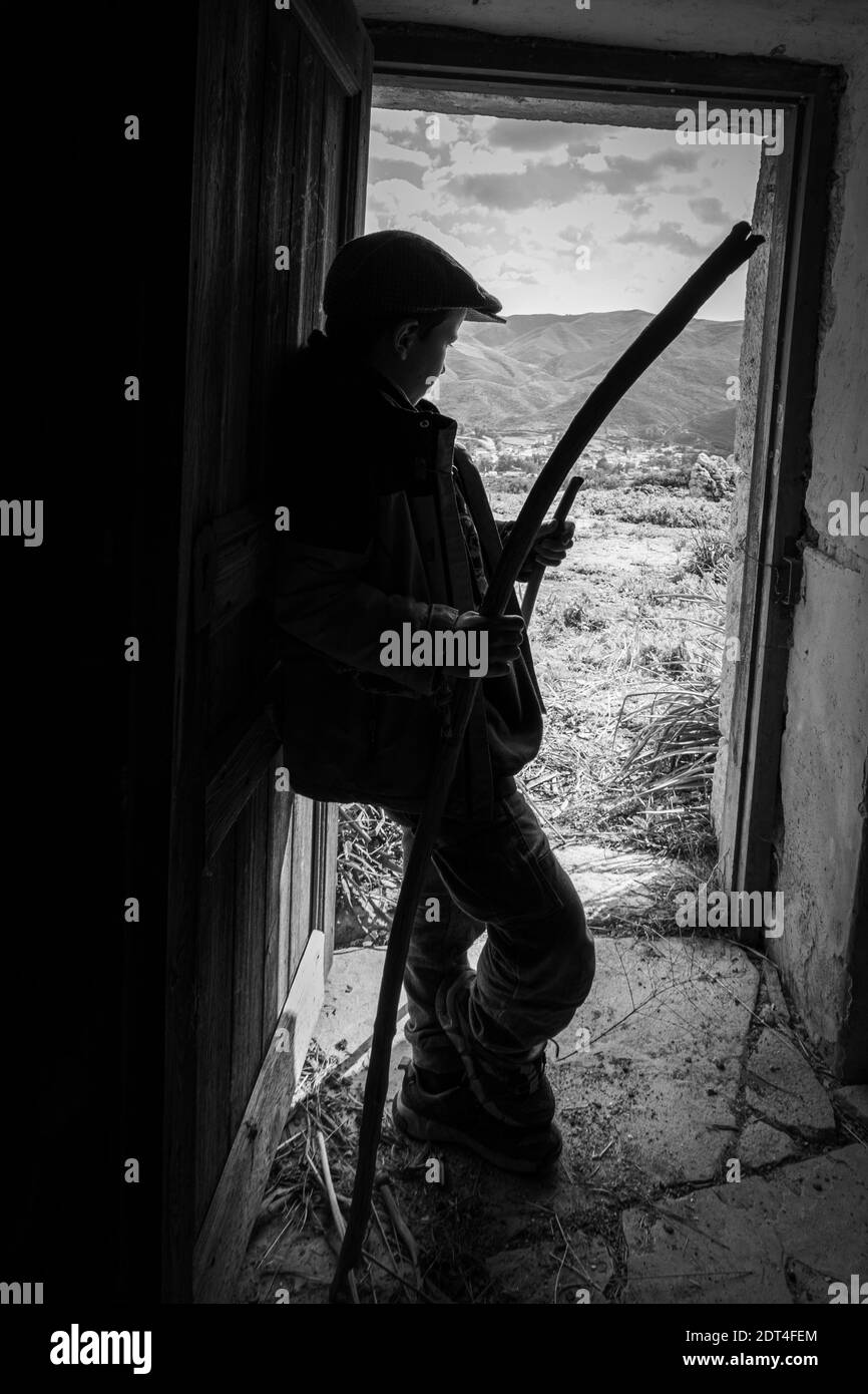 Schwarz-weiße Ansicht des Jungen, der an der Tür steht und hält Stick Stockfoto