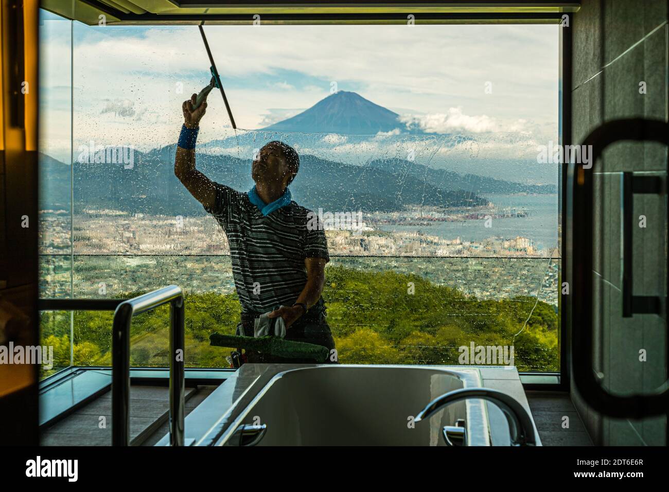 Ein Mitarbeiter reinigt das Panoramafenster des Badezimmers von außen, mit Blick auf den Berg Fuji, im Nippondaira Hotel in der Nähe von Shizuoka, Japan. Stockfoto