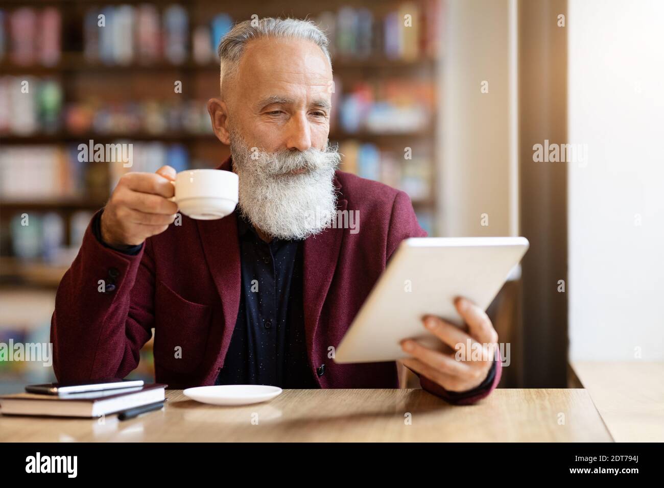Wohlhabender grauhaariger älterer Mann, der Kaffee trinkt und digitale Tablette benutzt Stockfoto