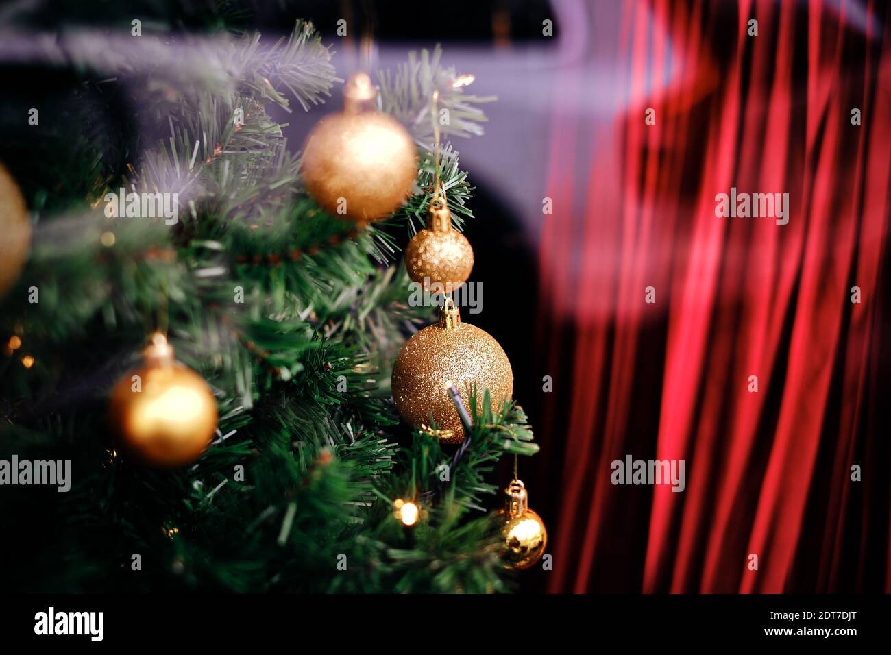 Magische grüne Kiefernzweige mit traditionellen, glänzenden, goldenen weihnachtsornamenten und einem roten verschwommenen Vorhang im Hintergrund. Stockfoto