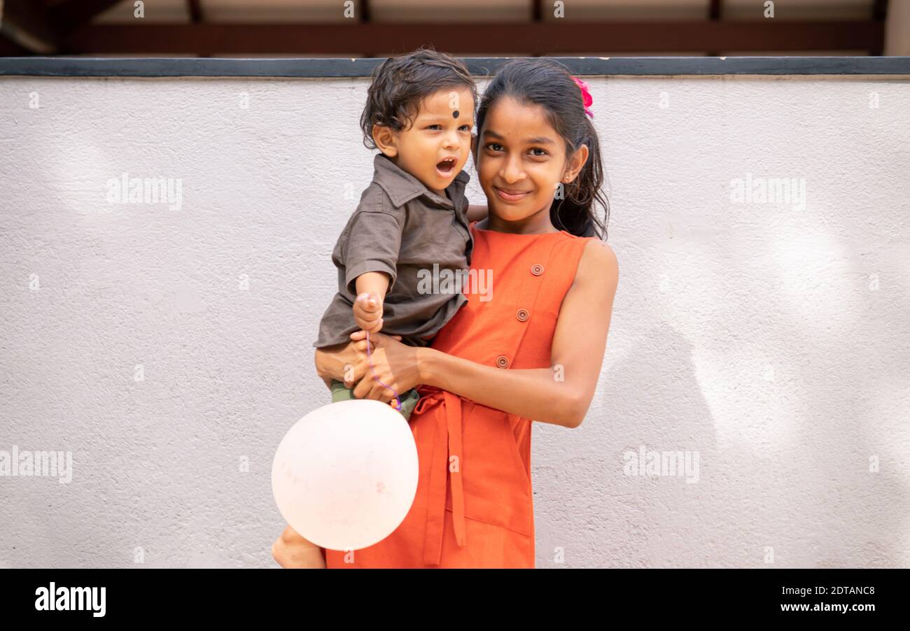 Ein 1-jähriger Junge und ihre ältere Schwester porträtieren im Freien, die Schwester hält ihren jüngeren Bruder und beide lächeln. Stockfoto