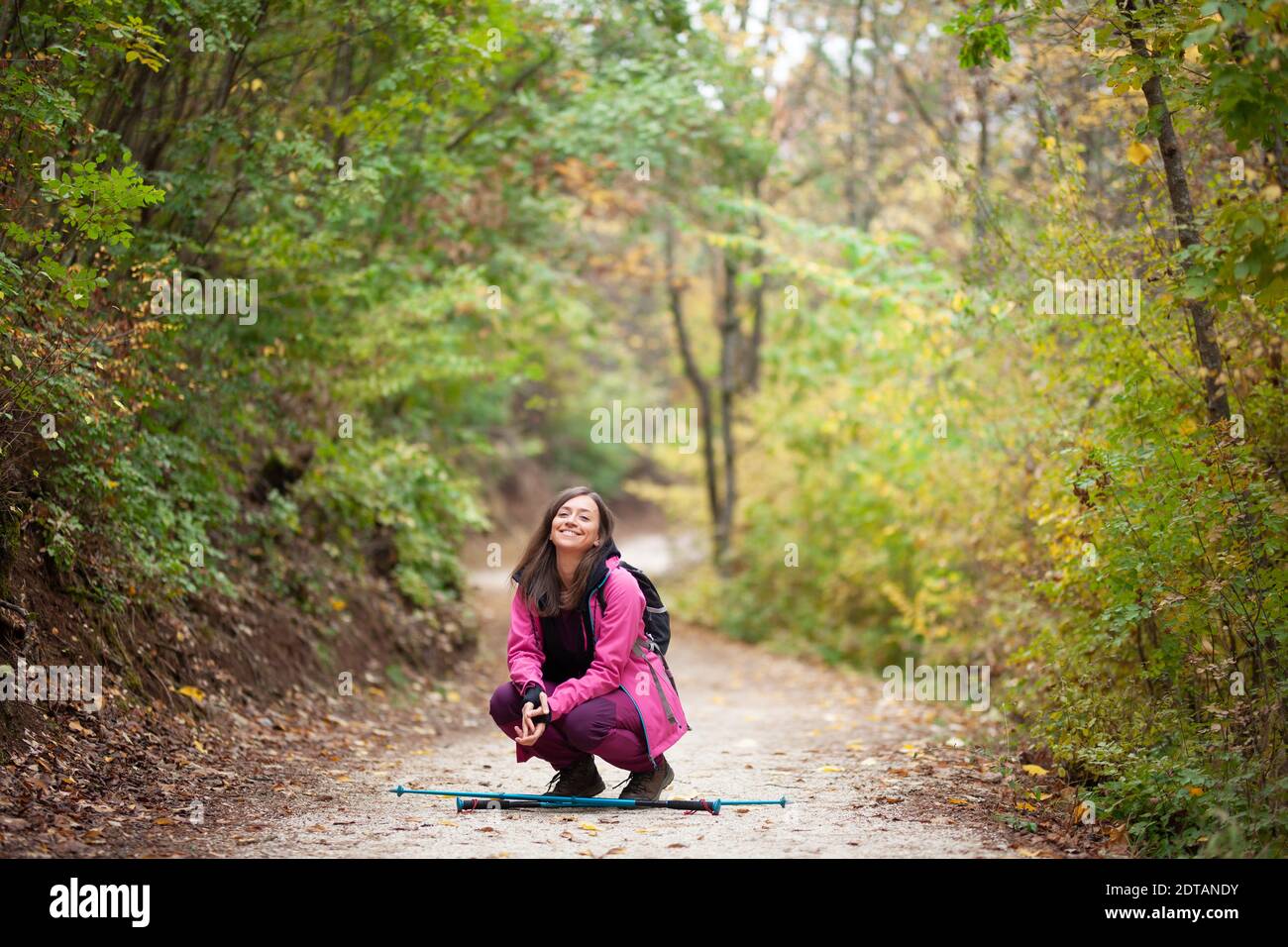 Hiker Mädchen hocken auf einem Weg in den Bergen. Rucksacktourist mit rosa Jacke in einem Wald. Gesunder Fitness-Lebensstil im Freien. Stockfoto