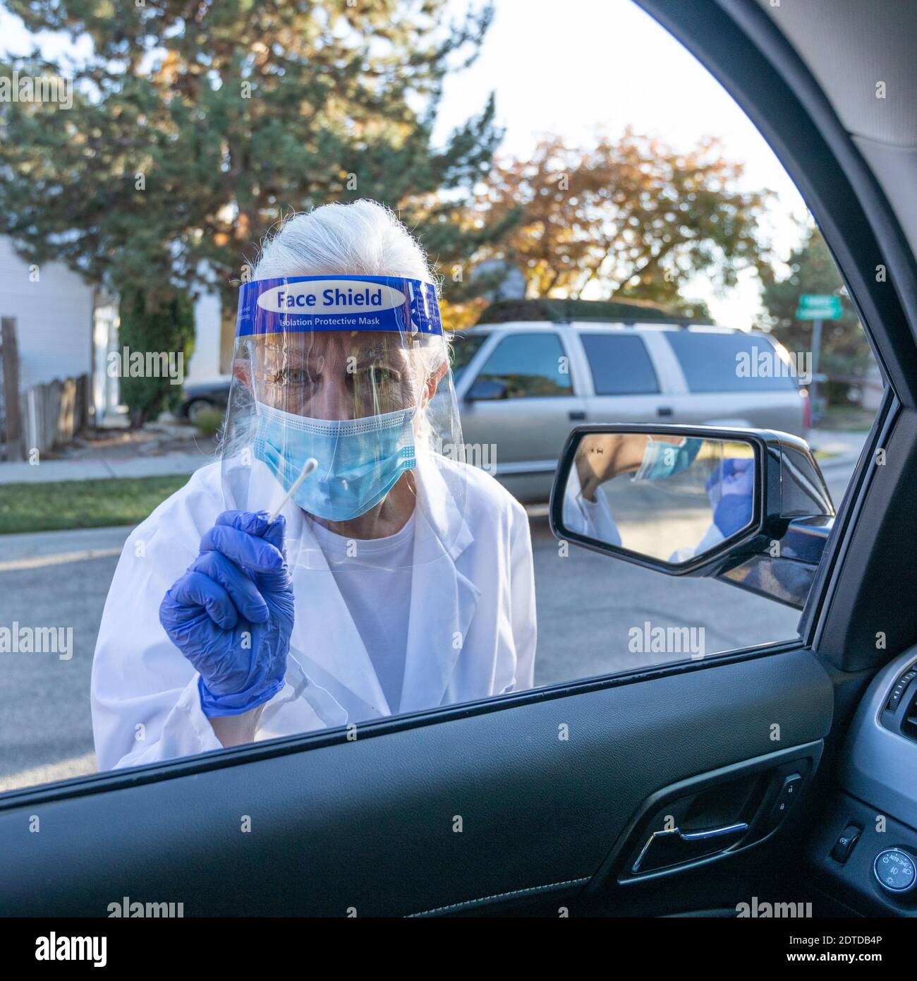 Medizinisches Personal in Schutzkleidung nähert sich dem Auto mit Coronavirus Abstrichtest Stockfoto
