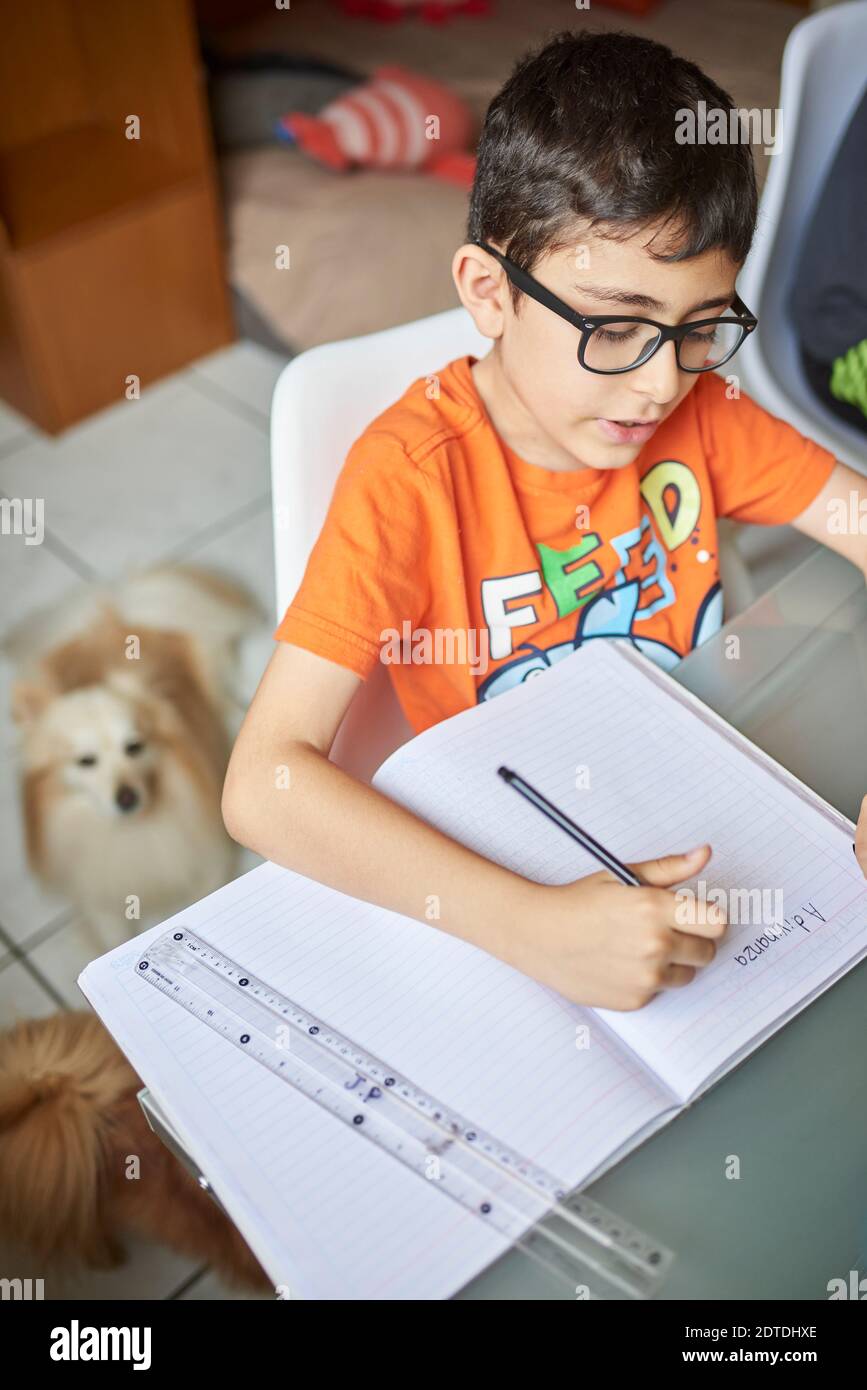 Jungen (8-9) schreiben im Notebook, während zu Hause lernen während Covid-19-Sperre Stockfoto