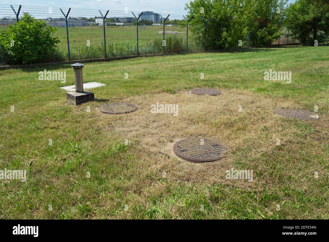 Gusseisen Kanalisation zwischen dem Gras. Metallabdeckungen für Abwasserkanäle an einem großen Verteiler Stockfoto