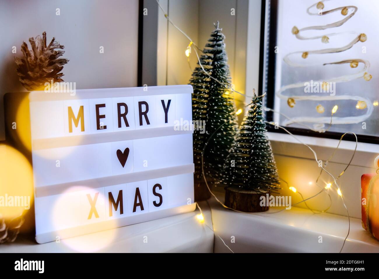 Lightbox mit Text FROHE WEIHNACHTEN weihnachten auf Fensterbank. Neujahr  Dekorationen, Girlande Lichter und weihnachtsbäume. Fenster mit Schneespray  bemalt. Hygge Stockfotografie - Alamy