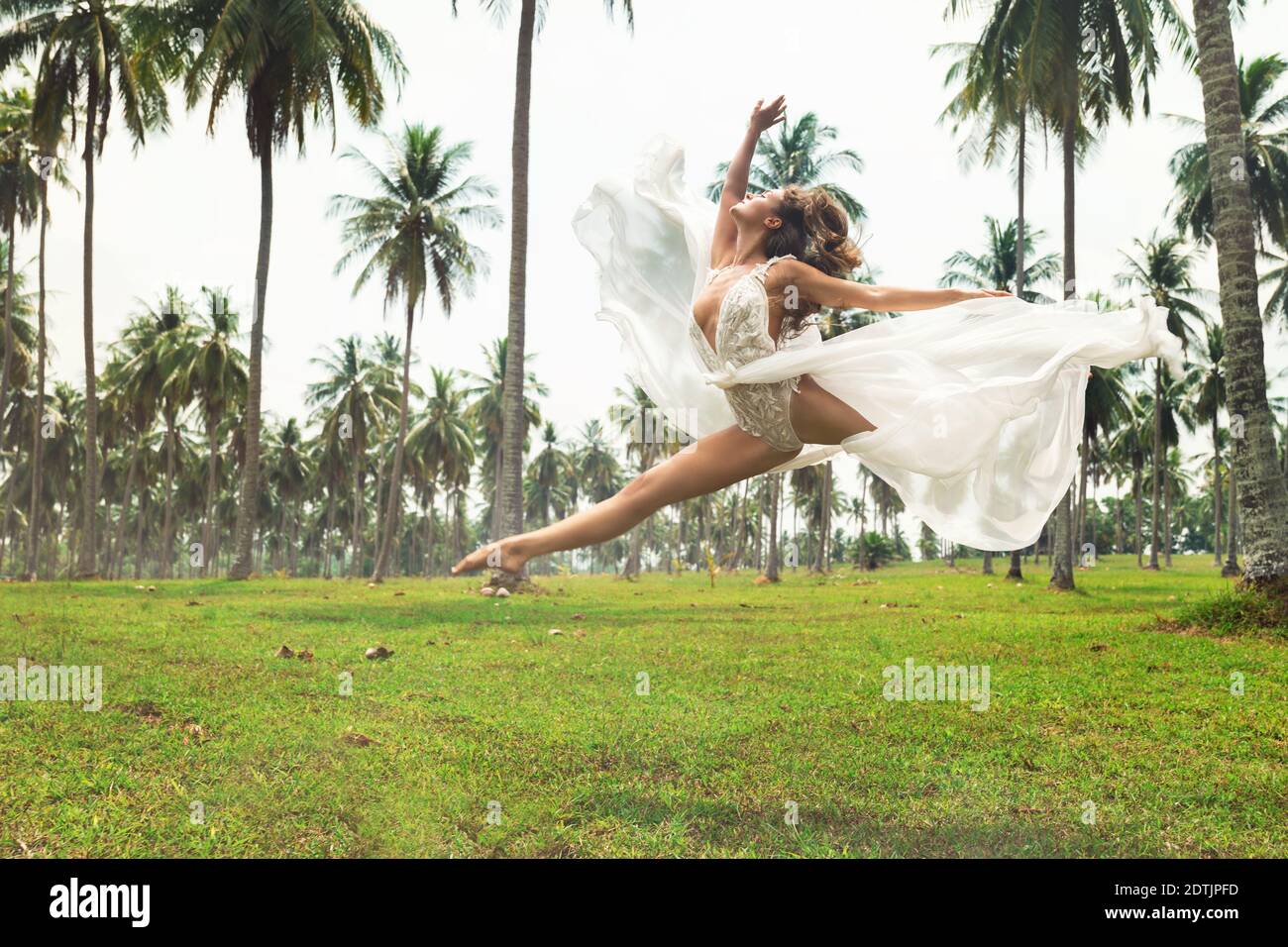 Glückliche Braut in schönen Hochzeitskleid ist so aufgeregt und glücklich. Sie springt im Tanz auf dem Feld mit vielen Palmen Stockfoto