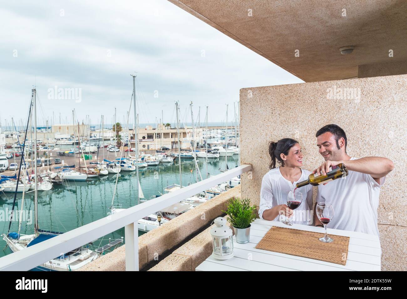 Glückliches junges Paar lächelt und trinkt Rotwein auf der Terrasse am Yachthafen. Paarbeziehung und Lifestyle-Konzept. Stockfoto