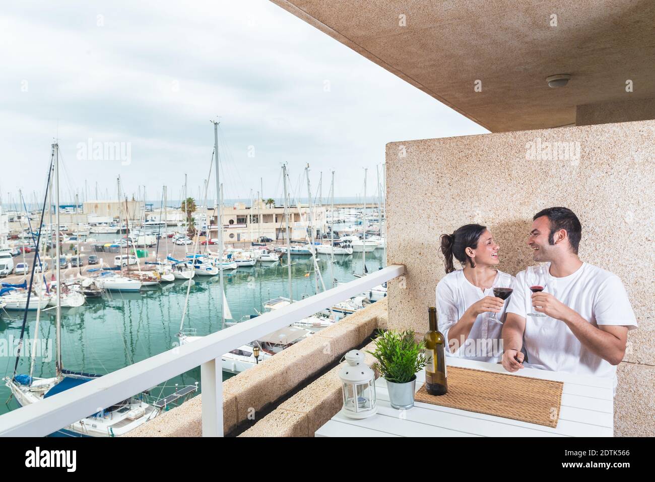 Glückliches junges Paar lächelt und trinkt Rotwein auf der Terrasse am Yachthafen. Paarbeziehung und Lifestyle-Konzept. Stockfoto