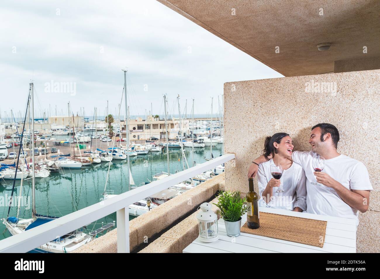 Glückliches junges Paar lächelt und trinkt Rotwein auf der Terrasse am Yachthafen. Paarbeziehung und Lifestyle-Konzept. Stockfoto