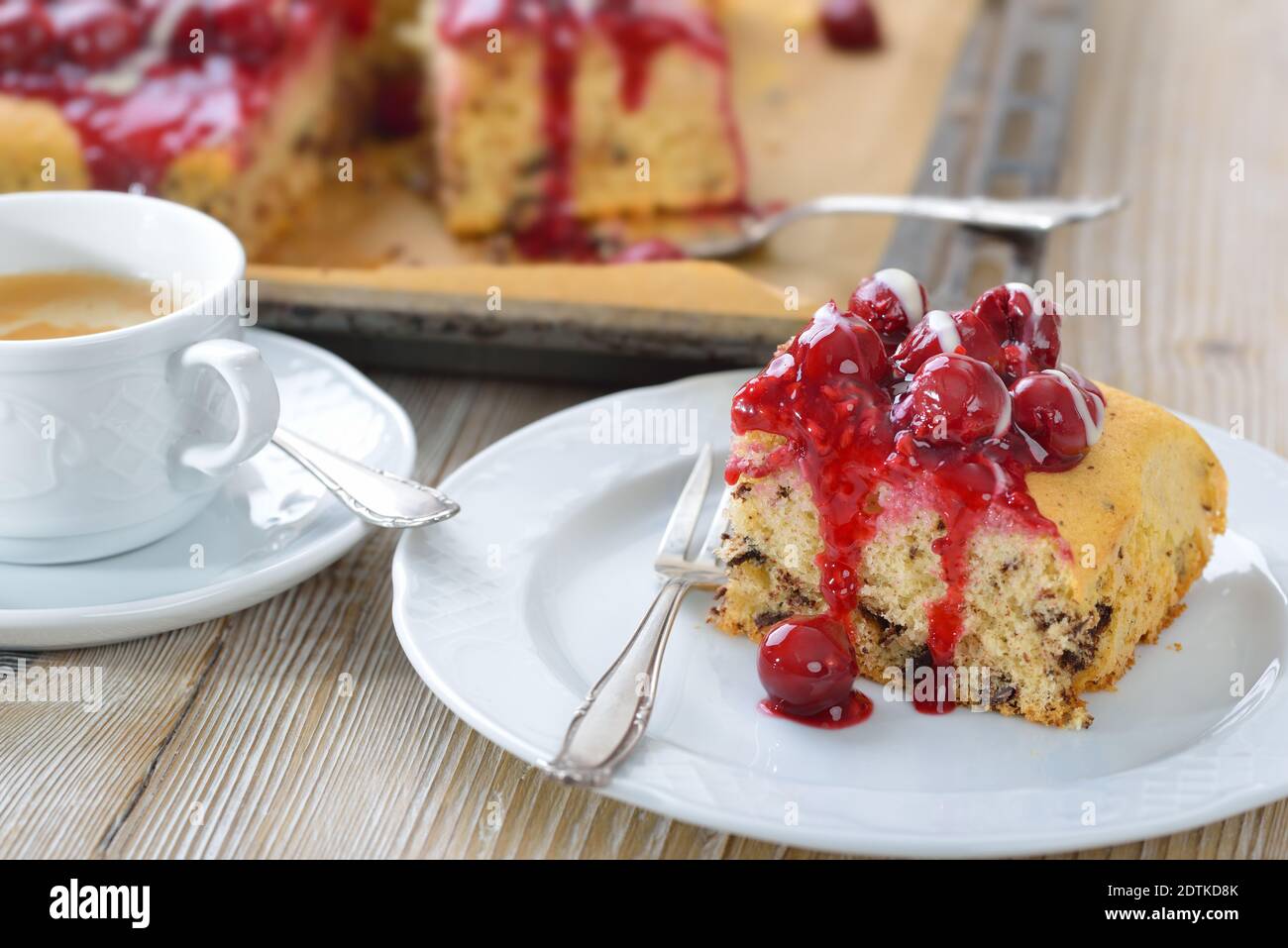 Süßer Stracciatella Kuchen mit rotem Fruchtgelee, Kirschen und Vanillesauce bedeckt, serviert mit Kaffee Crema Stockfoto