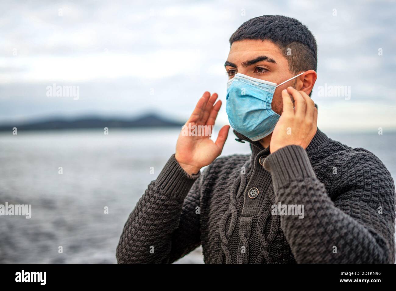 Schöner Kerl in dunkler Wolle Pullover im Freien in Sea Resort Hat gerade Gesicht medizinische Schutzmaske gegen Coronavirus Pandemie getragen Virus - junger Mann Livi Stockfoto