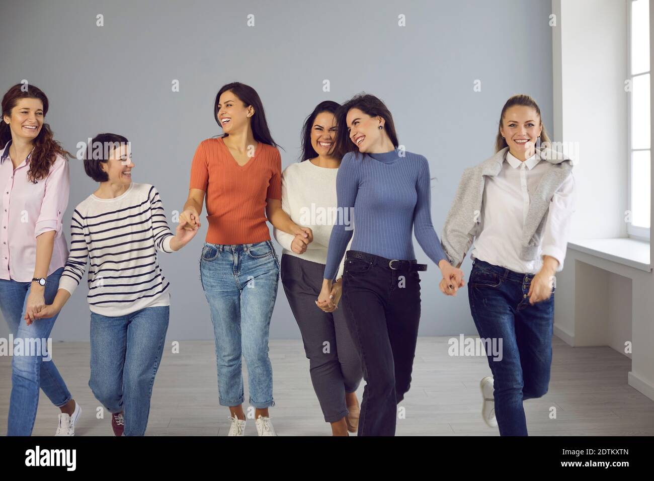 Eine Gruppe glücklicher Frauen, die Hand in Hand gehen und gegenseitige Unterstützung und Solidarität zeigen Stockfoto