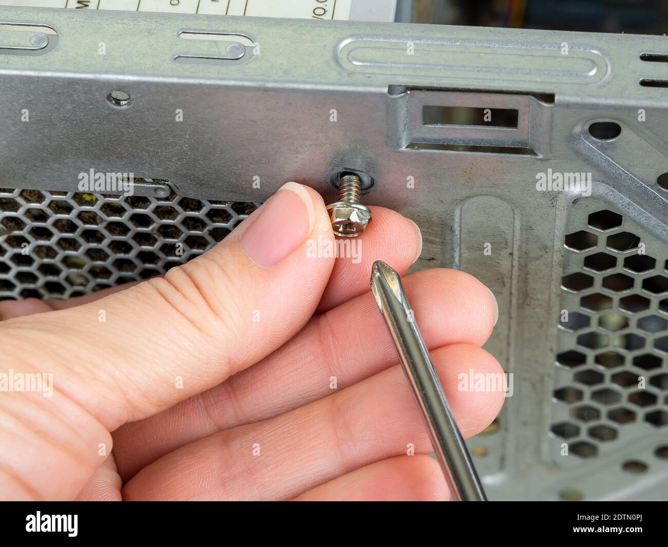 Mit den Fingern entfernen Sie die Schrauben, mit denen das Netzteil in einem Turmgehäuse befestigt ist, mit einem Schraubendreher. PC-PSU-Replasierung, Hardware-Ausrüstung. Stockfoto